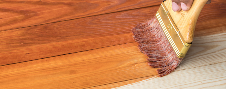 hand holding a brush applying varnish paint on treated pine